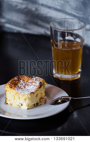 A slice of Ukrainian traditional cottage cheesecake and uzvar, a dried fruit compote, on a dark wooden table