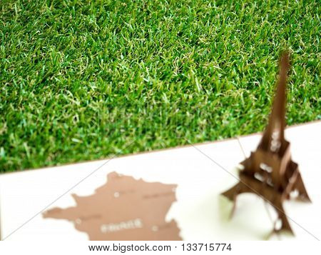 Artificial grass with blurry foreground of Eiffel tower paper model apply for European football tournament in France with copy space (selective focus)