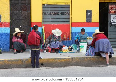 Cajamarca Peru - June 10 2016: Andean women sit on sidewalk and sell fruit in Cajamarca Peru on June 10 2016