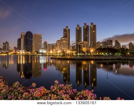 Night light with modern building and flower foreground in the park beside lake at Bangkok Thailand (Benchakitti Park)