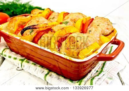Cutlets of turkey meat baked with red tomatoes and yellow pepper in a ceramic roasting pan on a towel, parsley on a wooden boards background