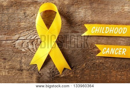 Yellow ribbon and text Childhood Cancer on wooden background