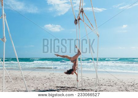 Pole dance outdoors. Young slim girl doing poledance on the beach over sea.