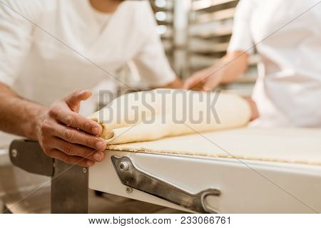 Cropped Shot Of Bakers Rolling Dough With Industrial Dough Roller At Baking Manufacture