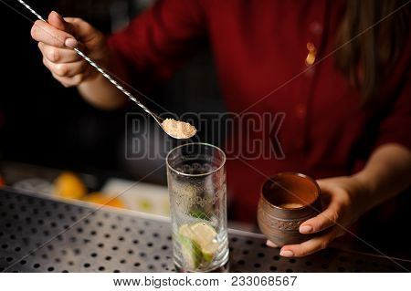 Female Bartender Putting A Spoon Of Cane Sugar Into A Glass At The Steel Bar Counter