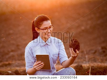 Pretty Young Engineer Woman Holding Earth Clod And Tablet And Researching Soil In Field