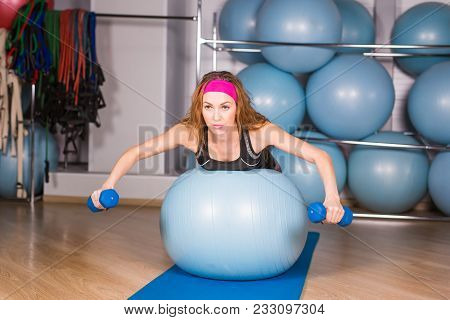 Woman Exercising With Dumbbells On A Fitness Ball.