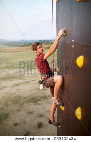 Sporty Man Practicing Rock Climbing In Gym On Artificial Rock Training Wall. Young Talanted Climber 