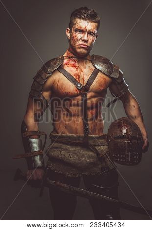 Bloody Gladiator In Armor Holding Sword. Isolated On Grey Background.