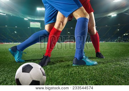 Football Players Tackling For The Ball Over Green Grass At Stadium. Professional Football Soccer Pla