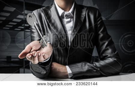 Cropped Image Of Businessman In Suit Keeping Stone Key Symbol In Hand With Dark Office View On Backg