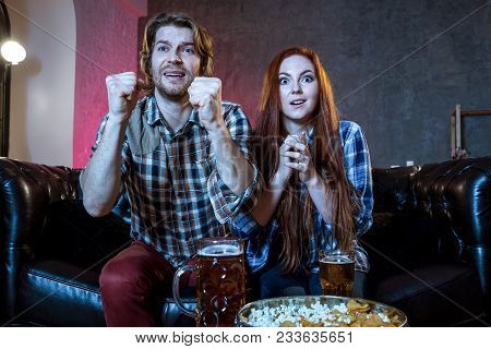 Young Couple Cheering For A Sport Team Watching Sports On Tv. They Are Screaming And Gesturing For A