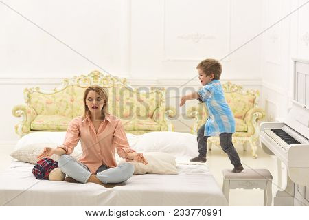 Young Parent Meditating, While Little Son Near Piano, Annoying Mom. Kid Annoyed Mother With Noise. M