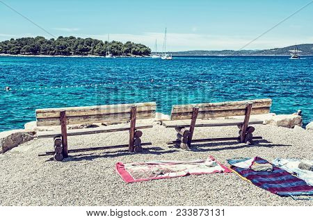 Wooden Benches And Towels On The Beach, Solta, Croatia. Summer Vacation. Sea With Yachts Scene. Blue