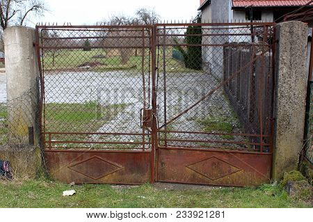 Rusted And Partially Twisted Metal And Wire Gates Locked With Chain And Small Padlock With Uncut Gra