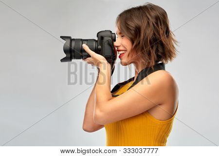 people and photography concept - happy woman photographer in mustard yellow top with digital camera over grey background