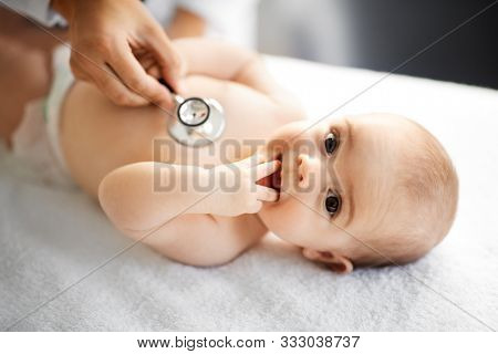 medicine, healthcare and pediatrics concept - close up of female doctor with stethoscope listening to baby girl's patient heartbeat or breath at clinic or hospital