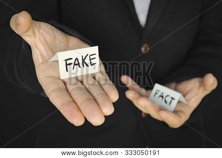 A Piece Of Paper With The Inscription Fake In A Mans Hand On The Background Of Another Hand With The