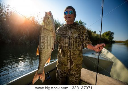 Happy fisherman holds the trophy Asp fish (Leuciscus aspius) and smiles