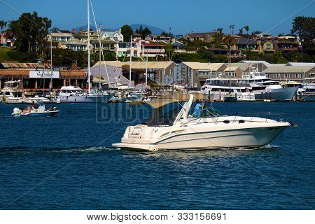August 25, 2019 In Newport Harbor, Ca:  Motor Boat Riding Out To Sea With Yachts Docked In Front Of 