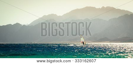One Surfer Rides In The Red Sea Against The Backdrop Of A Rocky Coast In Egypt In The Evening