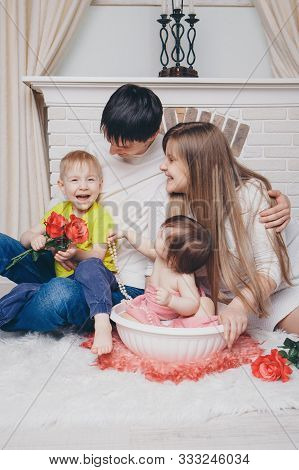 A Little Girl With Family Is Bathing In A Bath With Flowers By The Fireplace. A Child Washes In A Ba