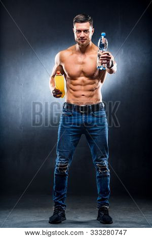 Shirtless Athletic Muscular Guy Holding Bottles With Still Drinks In Hands On The Dark Grey Bachgrou
