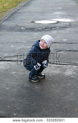 Funny Toddler Boy On A Walk In Autumn. Smiling Child Wearing White Hat, Blue Jacket, Woolen Mittens 