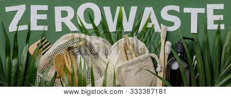 Zero waste concept. Cotton bag, bamboo cultery, glass jar, bamboo toothbrushes, hairbrush and straws on green background