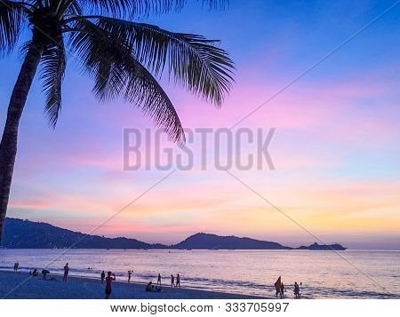 Palm Trees And The Sea With Tourists At Sunset