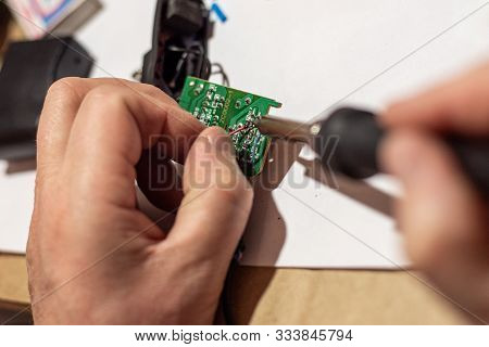 The Hands Of The Worker Hold A Soldering Iron, With Which He Solders The Wiring In The Electronic Ci