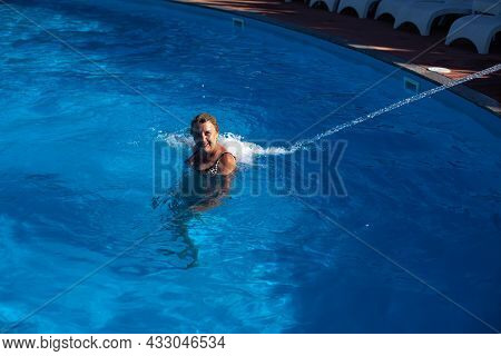 An Adult, Smiling Woman Enjoys A Hydro Massage Of The Back And Neck With A Jet Of Water In The Pool 
