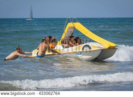 Family On A Marine Pedal Catamaran Trying To Land Across The Waves At Marina San Nicola Beach In Ita