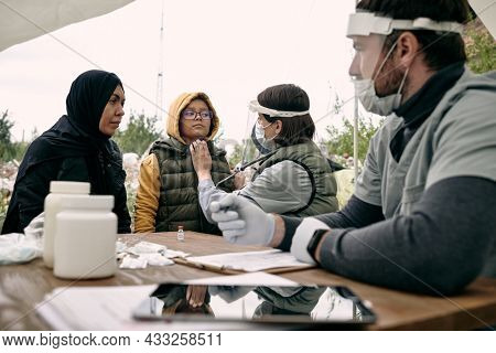 Medical specialist examining health of girland talking to her muslim mother outdoors