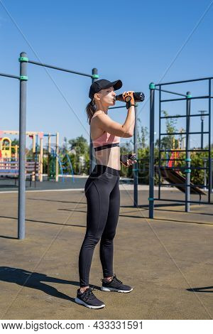 Young Sportive Woman In Sport Gloves Drinking Water On Sport Ground