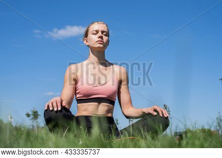 Sportive Woman Meditating Sitting On Grass Under Blue Sky
