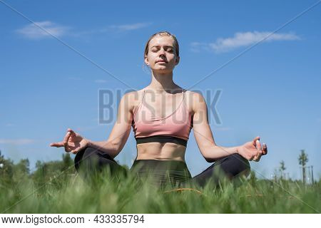 Sportive Woman Meditating Sitting On Grass Under Blue Sky