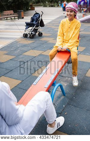 Smiling Arabian Boy In Kufiya Playing With Blurred Father On Playground