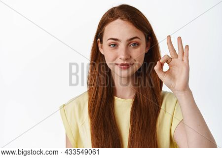 Portrait Of Smiling Redhead Woman Looks Confident, Shows Okay Zero Sign, No Proble Gesture, Assure Y