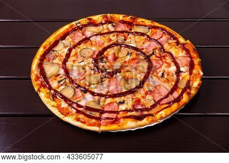 A Whole Rustic Pizza With Pickled Cucumber, Sousages, Bacon And Barbecue Sauce