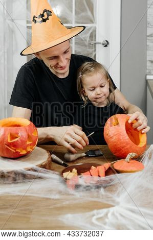 Parent With Chld Are Carving Jack O Lantern From Pumpkin For Halloween At Home. Father In Hat Prepar
