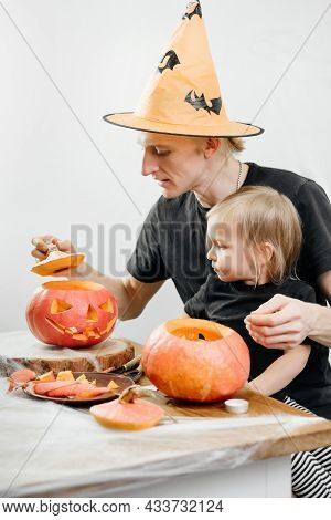 Parent With Chld Are Carving Jack O Lantern From Pumpkin For Halloween At Home. Father In Hat Prepar