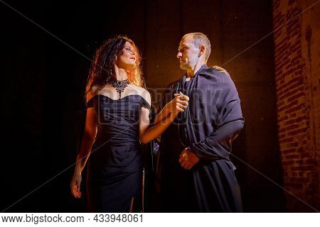 A Couple In Old Dark Clothes In An Abandoned Castle With Old Brick Walls. A Man And A Woman Posing I