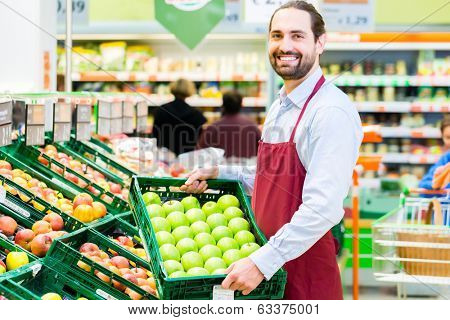 Supermarket clerk filling up apple storage racks in fruit department 