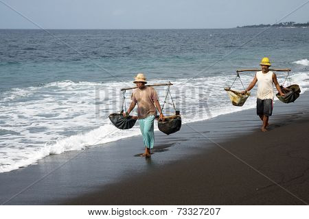 SEPTEMBER 18, 2014 - BALI, INDONESIA: Workers carry bags of sea water to bring inland to saturate the sand to make natural sea salt. Making natural sea salt is a traditional cottage industry here.