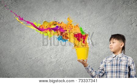 Young boy splashing colorful paint from bucket