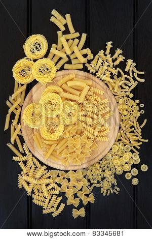 Pasta selection on a wooden board and loose over dark wood background.