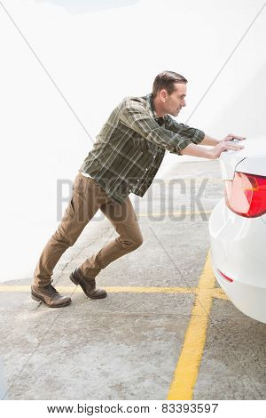Man pushing his broken down car in a car park
