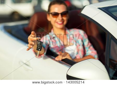 Young pretty woman sitting in a convertible car with the keys in hand - concept of buying a used car or a rental car