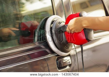 hands holding a power buffer machine cleaning a car.